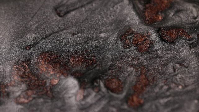 Close-up view of dark silver and copper paint swirling slowly and mixing to create abstract organic shapes, emphasizing a sandy texture and shimmering particles that form complex fluid patterns
