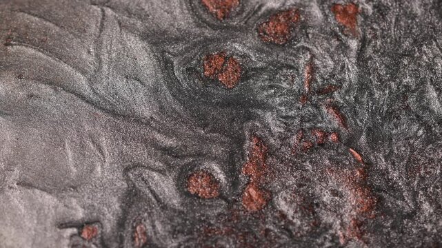 Close-up shot of dark titanium paint specialized sandy texture and radiant bronze particles on surface flowing and forming abstract swirling patterns