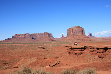 Monument Valley Vista: A breathtaking panoramic view unfolds across the vast expanse of Monument Valley, the iconic sandstone buttes stand proudly under a clear azure sky, showcasing nature's majesty.