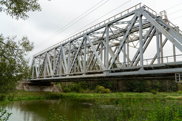Fototapeta premium massive white steel truss railway bridge spanning across a calm river surrounded by lush green forest