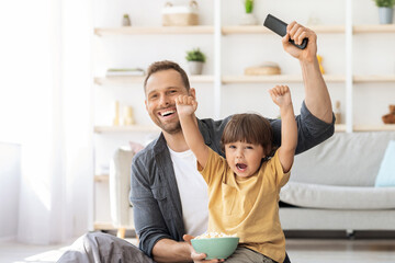 Little sport supporter. Positive young father watching football game on tv with his little son, emotional boy shouting enjoying goal of favorite team, free space © Prostock-studio