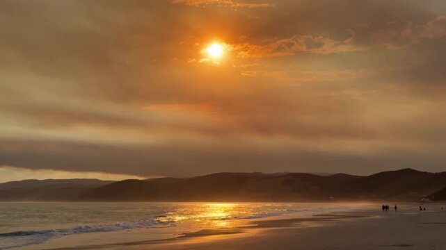 People walking along Fairhaven Beach, Australia during sunset. Ocean, mountains, and warm natural light create a calm coastal landscape.