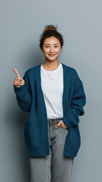 smiling woman in blue cardigan pointing up at copy space on teal wall friendly explainer portrait and marketing concept