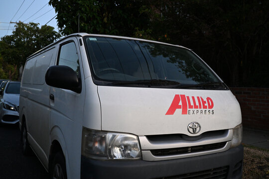 Slightly damaged Allied Express transport company logo on the front of a white Toyota HiAce van, in a suburban street during the evening