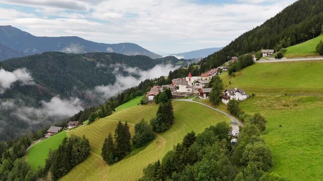 Forward drone flight, cinematic, bird view towards small Italian town in the mountains, town Eores (Afers) near Bressanone (Brixen). Cloudy summer day. View on the Church of San Giorgio in the centre