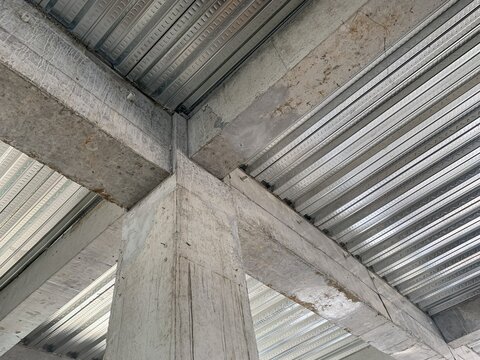 Structural detail of concrete beams and columns intersecting with corrugated metal decking, illustrating modern construction techniques in commercial building frameworks.