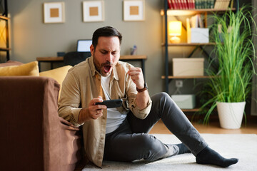 Obraz premium Man playing mobile game cheering victory at home