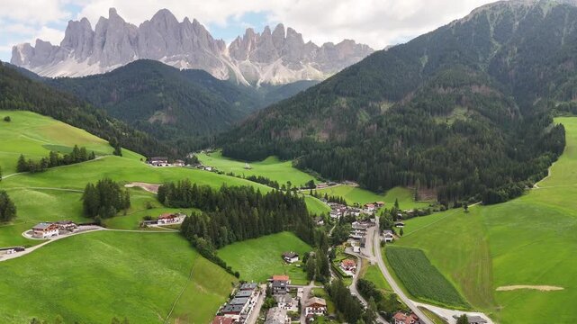 Forward drone flight, bird view, toward the beautiful village of St Magdalena, Val di Funes in South Tyrol. Wonderful valley with impressive Dolomites, sharp peaks in background. Summer travel destina