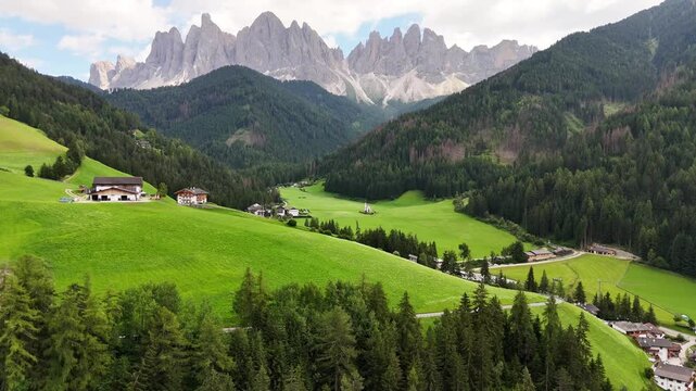 Forward drone flight, bird view, toward the beautiful village of St Magdalena, Val di Funes in South Tyrol. Wonderful valley with impressive Dolomites, sharp peaks in background. Summer travel destina