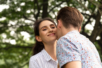 Fototapeta premium happy young couple in love relationship having romantic moment in the park. Caucasian man kissing his smiling wife.