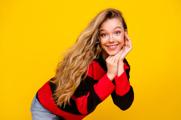 Charming young woman in a red and black sweater posing joyfully against a bright yellow background...