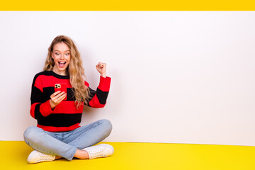 Young cheerful female in stylish apparel holds a smartphone and enjoys an exciting moment against...