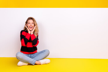 Cheerful young woman in casual trendy striped sweater sitting on a yellow background exuding...