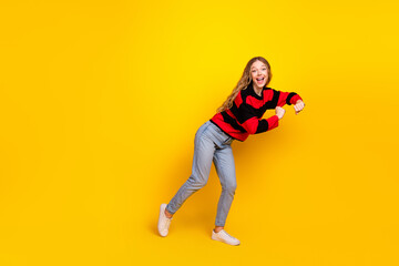 Cheerful young woman in trendy striped sweater dancing on vibrant yellow background embodying joy...