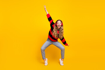Cheerful young woman in trendy striped sweater posing energetically against vibrant yellow...