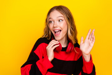 Adorable young woman in striped sweater with headphones posing cheerfully against bright yellow...