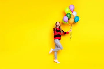 Fotobehang Onderzeeër Cheerful young woman wearing casual striped sweater and jeans posing with colorful balloons on a vibrant yellow backdrop  © deagreez
