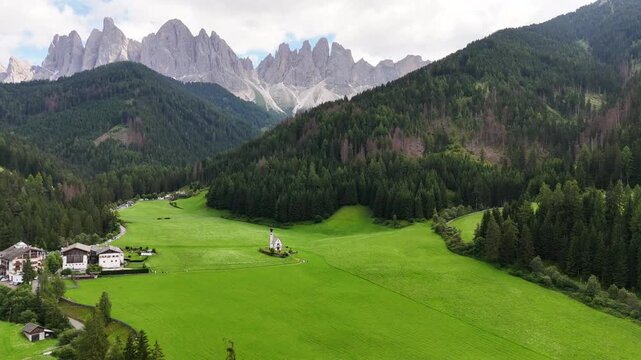 Drone flight, bird view, toward church of San Giovanni in Ranui near beautiful village of St Magdalena, Val di Funes, South Tyrol. Wonderful valley with impressive Dolomites, sharp peaks. travel desti