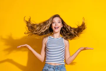 Fotobehang Onderzeeër Joyful young woman with wavy hair and striped top against a vibrant yellow background exudes happiness  © deagreez