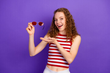 Playful young woman with striped top and sunglass posing against purple background