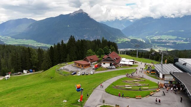 22 july 2024, Imst, Austria. Forward drone flight at U-alm, untermarkter alm, with arrival of the gondola lift at the mountain. Touristic place, people walking on hiking trail, terrace parasols. Mount