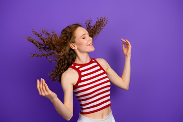 Young woman with red hair wearing a striped top dances against a purple background