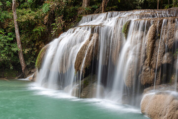 Obraz premium Erawan Falls cascading down rocks in lush jungle. Located in Erawan National Park, Thailand. Tropical landscape with flowing water and green surroundings.