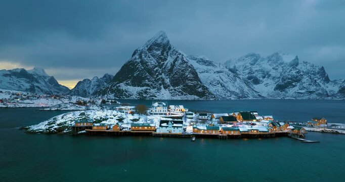 Sakris&oslash;y zur blauen Stunde, gelbe Fischerh&uuml;tten am ruhigen Fjord vor schneebedeckten Bergen, kalte Abendstimmung mit klarem arktischem Licht auf den Lofoten in Norwegen