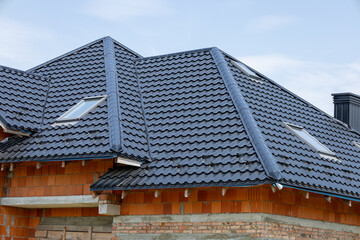 Workers enhance the charm of a suburban house as they install a sleek black tiled roof on a sunny day, adding style and protection