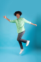 Joyful black guy jumping up in the air and showing funny figures, showing positive emotions over...