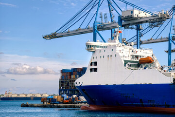 Naklejka premium Birzebbuga, Malta – maritime industrial facility with ship, heavy-duty cranes and freight port infrastructure in sunshine
