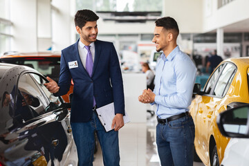 Wealthy middle-eastern young man choosing new car, having conversation with friendly sales manager...