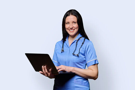Female nurse holding laptop, looking at camera on white studio background