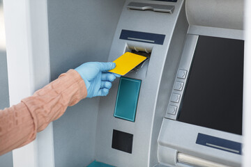 Cropped young islamic female in rubber glove inserts credit card into ATM to withdraw money outdoor, close up, empty space. Finance management, cash, bank service, new normal during covid-19 outbreak