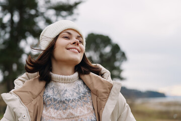 Obraz premium Woman outdoors in a cozy beanie and jacket, smiling with the breeze in a natural landscape, capturing warmth, happiness and carefree mood in fresh air.