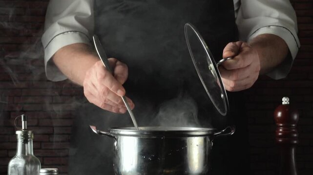 A chef in a black apron lifts the lid off a pot and ladles buckwheat, releasing steam against the backdrop of a rustic kitchen with various kitchen utensils