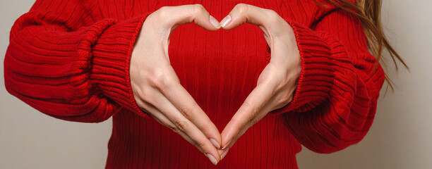 Frauenhände formen ein Herz vor einem roten Pullover