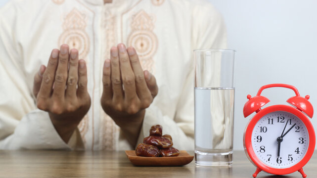 Doa berbuka puasa performed by a man with dates, water, and an alarm clock on the table. A spiritual moment of breaking the fast during Ramadan, highlighting Islamic traditions and worship