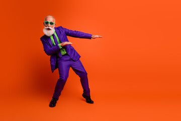 Energetic elderly man in purple suit dances in bright orange studio with green shirt creating joyful retro style