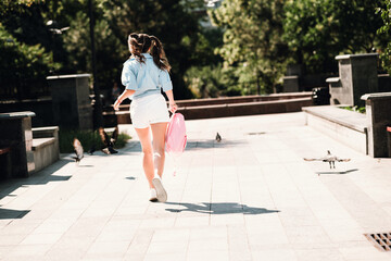 Young girl walks away in a sunny city park carrying a pink backpack enjoying a casual day outdoors...