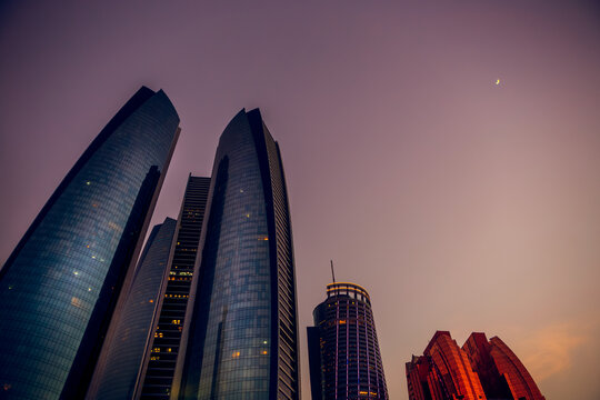Low angle view of modern skyscrapers at dusk with a crescent moon, Abu Dhabi, United Arab Emirates