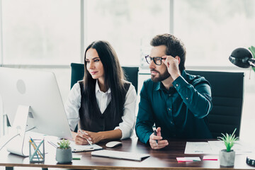 Two professionals at a modern office collaborate over documents and a computer during a business meeting