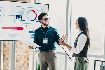 Two professionals present a project during a dynamic office presentation with charts on a large screen and engaging discussion