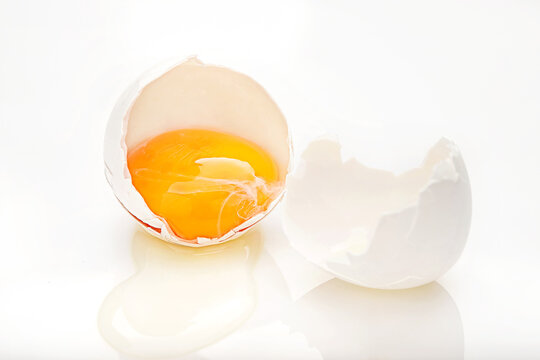 Close-up of a cracked egg with an egg yolk in a halved eggshell and the egg white spilling onto the table