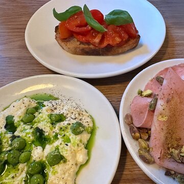 Close-up of three plates with tomato bruschetta, mortadella with roasted pistachio nuts and Stracciatella cheese with beans and basil oil on a table
