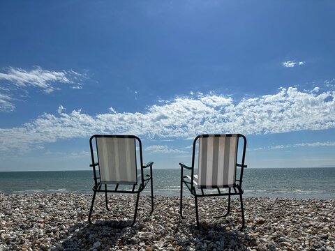 Two folding garden chairs on a shingle beach, West Wittering, West Sussex, England, UK