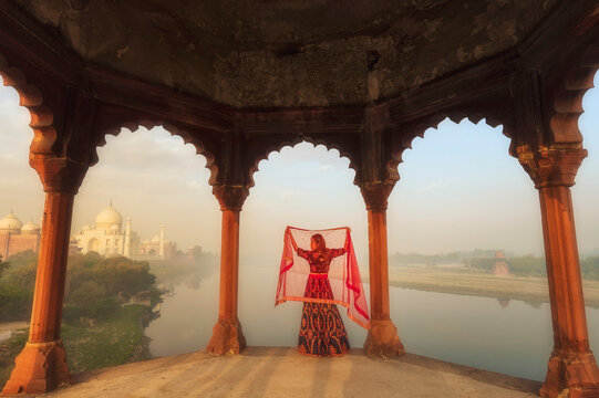 Rear view of a Young Woman standing by the Jamuna river holding a shawl above her head at sunset, Taj Mahal, Agra, Uttar Pradesh, India,