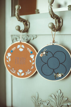 Two embroidered embroidery hoops with floral motifs hanging on vintage furniture hooks