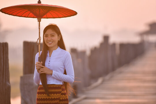 Portrait of a smiling young Woman carrying a traditional parasol standing on U Bein Bridge, Amarapura near Mandalay, Myanmar