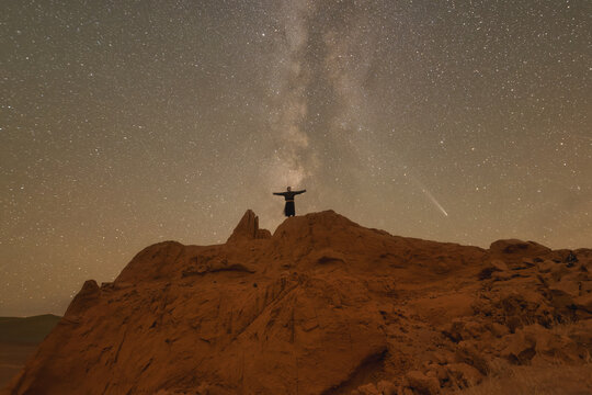 Milky Way over a person standing on desert rocks with outstretched arms, Western Mongolia, Mongolia